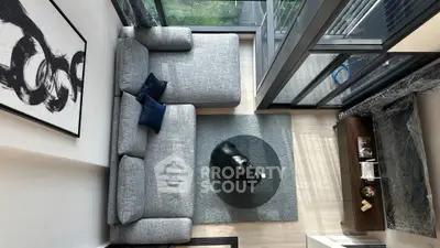 Modern living room with large windows and stylish decor, featuring a cozy gray sofa and chic artwork.