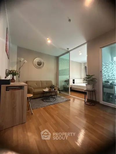 Modern living room with wooden flooring and glass partition leading to bedroom, featuring stylish decor.