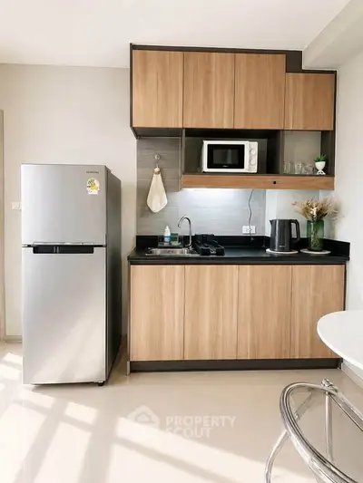 Modern kitchen with sleek cabinets, stainless steel fridge, and microwave in a compact layout.
