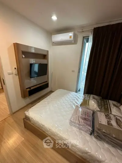 Modern bedroom with wall-mounted TV and air conditioning, featuring a cozy bed and wooden flooring.