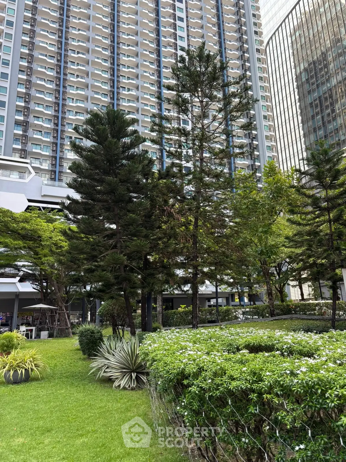 Lush garden area in front of a modern high-rise building with tall trees and manicured lawns.