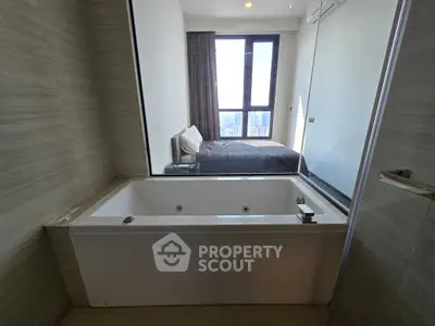 Modern bathroom with luxurious bathtub and view into a stylish bedroom with large window.