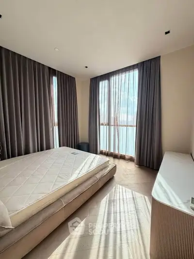 Spacious bedroom with large windows and elegant curtains, offering abundant natural light and a serene atmosphere.