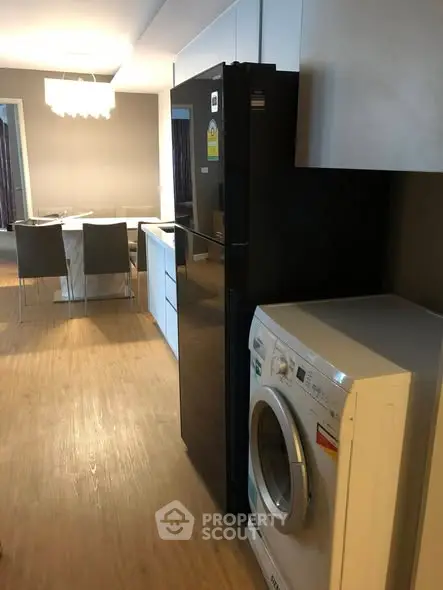Modern kitchen with sleek appliances and dining area, featuring a washing machine and fridge.