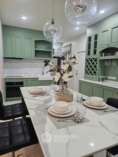 Elegant kitchen with green cabinets, marble countertop, and modern dining setup.