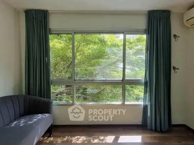 Bright living room with large window and lush green view, featuring elegant curtains and modern sofa.