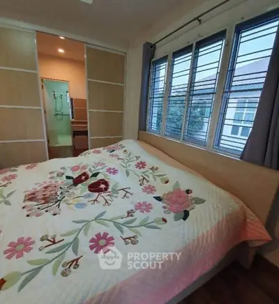 Cozy bedroom with floral quilt and large windows offering natural light.