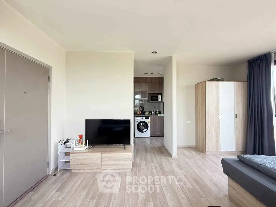 Modern apartment interior with open layout, featuring a cozy living area and compact kitchen with washing machine.