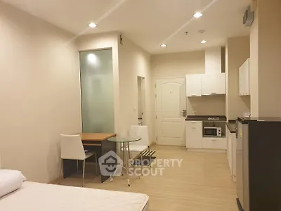 Modern studio apartment with open kitchen and dining area, featuring sleek white cabinetry and cozy lighting.