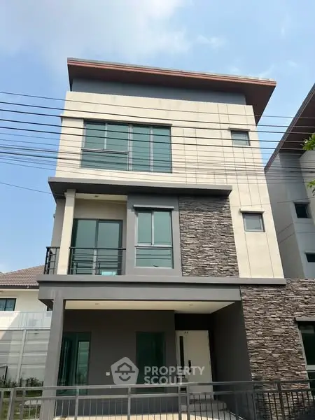 Modern three-story house with stone facade and large windows under a clear blue sky.