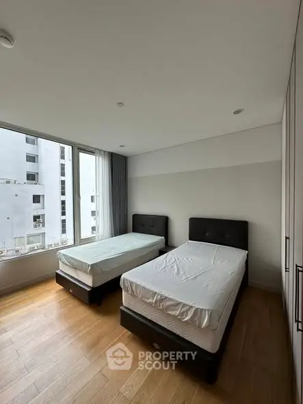 Spacious bedroom with twin beds and large window offering city view.