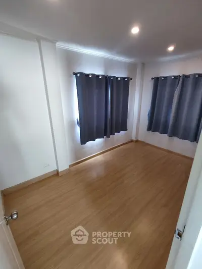 Spacious empty room with wooden flooring and dark curtains