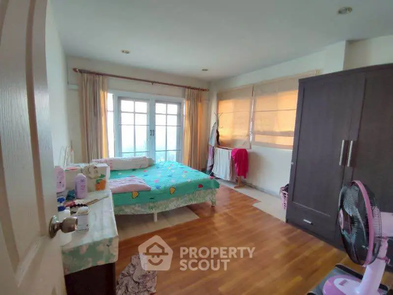 Cozy bedroom with wooden flooring and large windows offering natural light.