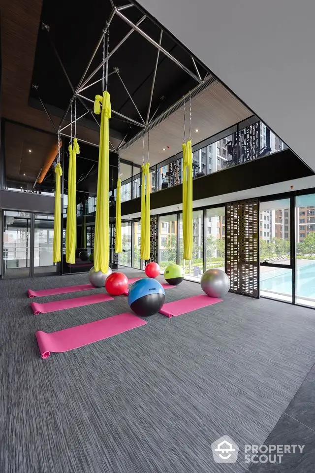 Modern gym with yoga mats and exercise balls overlooking a pool in luxury apartment complex.