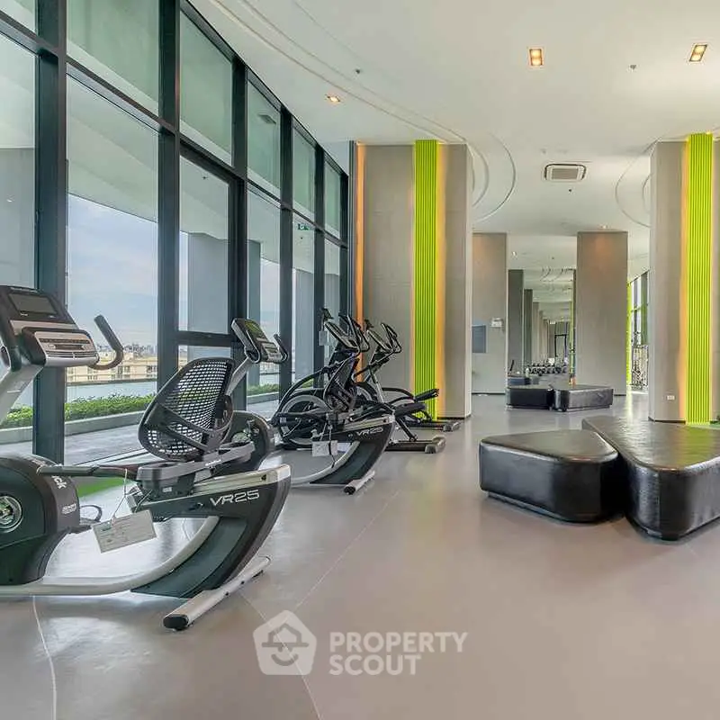 Modern gym with exercise equipment and large windows in luxury building.