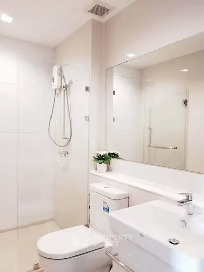 Modern bathroom with sleek fixtures and large mirror, featuring a glass shower enclosure and elegant white decor.