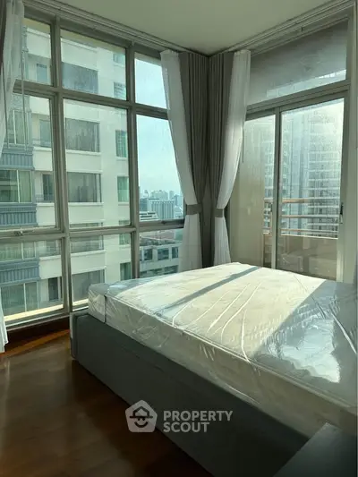 Spacious bedroom with large windows offering stunning city views in a modern apartment.