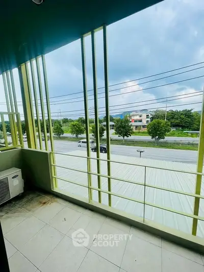 Spacious balcony with modern railing offering scenic road view and lush greenery.