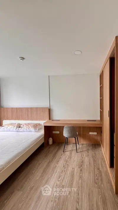 Modern bedroom with wooden flooring, built-in desk, and cozy bed setup.