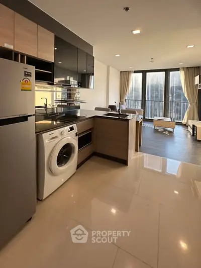 Modern open-layout kitchen with washing machine and spacious living area, featuring large windows and sleek design.