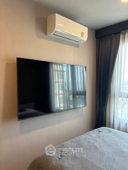 Modern bedroom with wall-mounted TV and air conditioning unit, featuring large window with curtains.