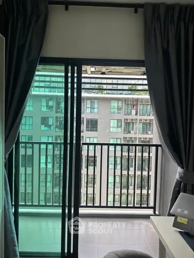 Modern apartment with balcony view overlooking neighboring building, featuring sleek sliding glass doors and elegant curtains.