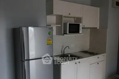 Compact kitchen with fridge, microwave, and sink in modern apartment.