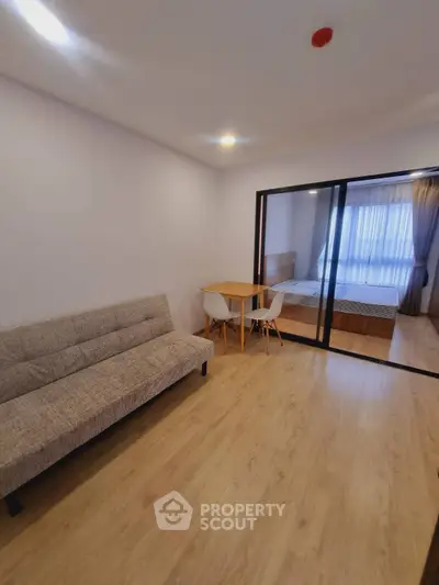 Modern apartment with cozy living room and bedroom separated by glass doors, featuring stylish furniture.