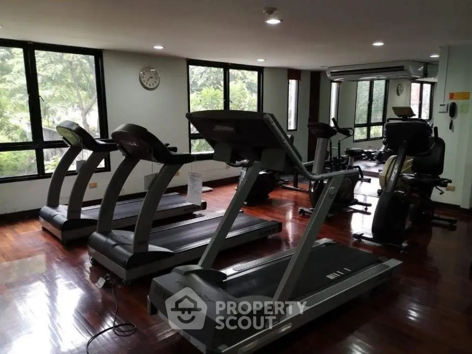 Spacious gym with modern equipment and large windows offering natural light.