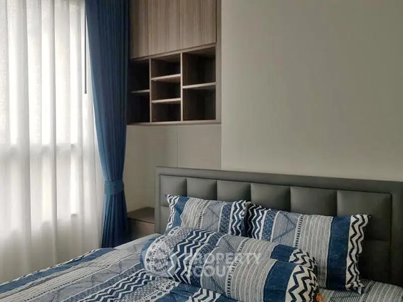 Modern bedroom with stylish bedding and built-in storage, featuring natural light from large window.