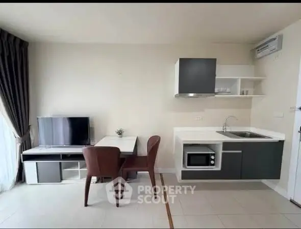 Modern compact living room with kitchenette, featuring sleek furniture and natural light.