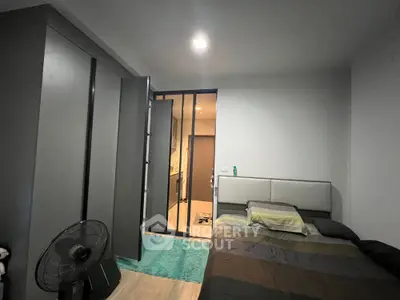 Cozy bedroom with modern design, featuring a large bed, sleek wardrobe, and a standing fan, leading to a well-lit ensuite bathroom.