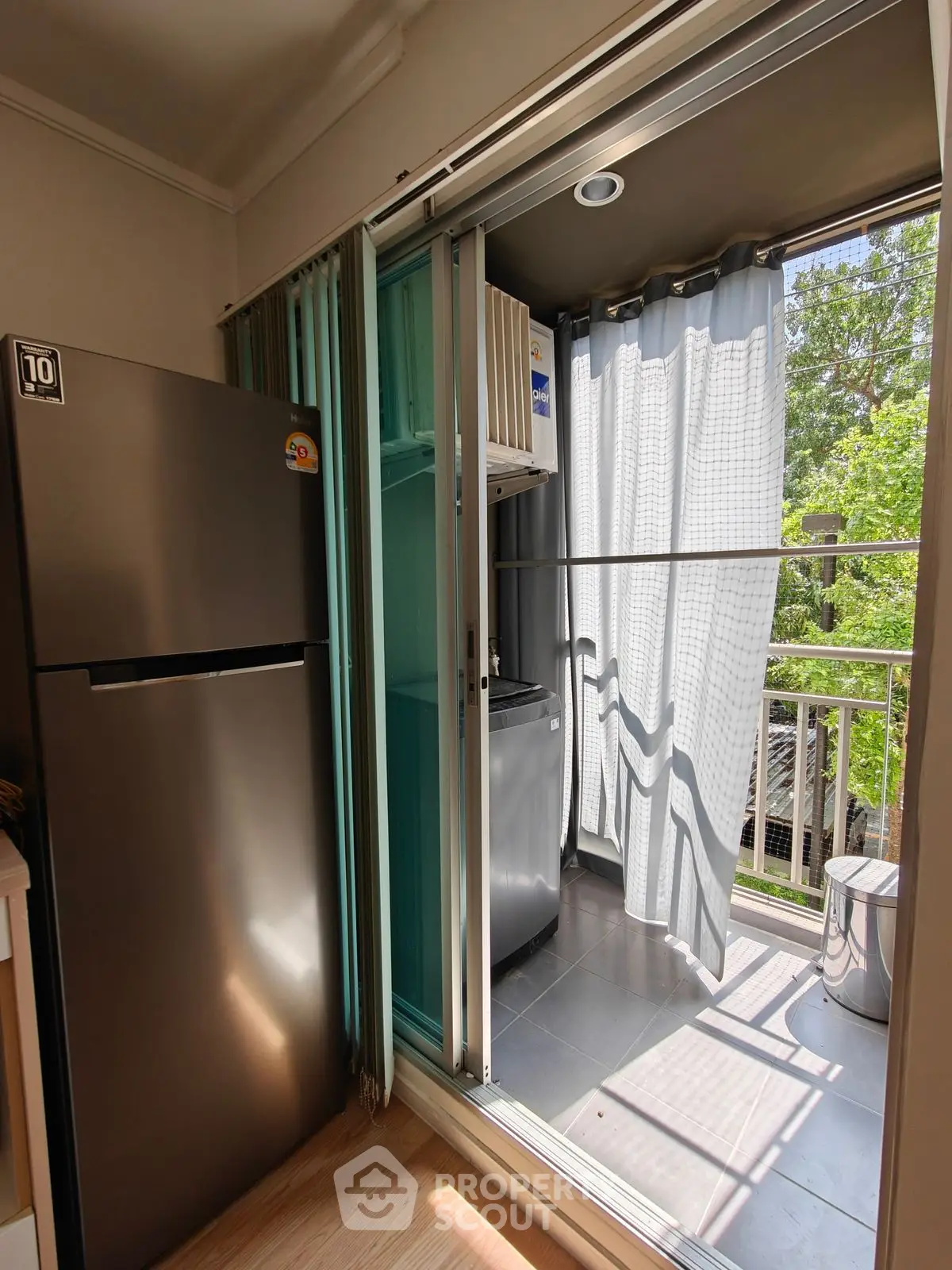 Modern balcony with sliding glass doors and appliances, overlooking lush greenery.