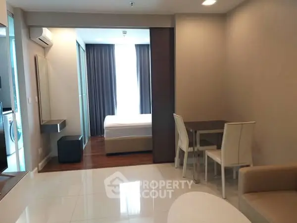 Modern open-plan living room with dining area and bedroom view in a stylish apartment.