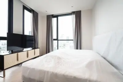 Modern bedroom with large windows offering city views, featuring a sleek TV stand and contemporary decor.