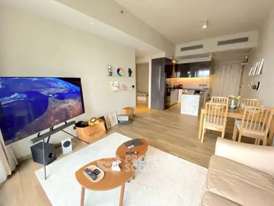 Modern living room with open kitchen, featuring stylish furniture and a large TV, perfect for entertainment.