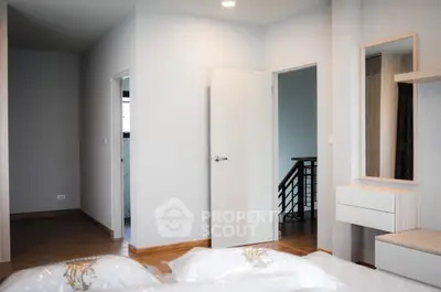 Modern bedroom with sleek design and wooden flooring, featuring a stylish mirror and open door to hallway.