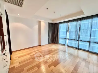 Spacious empty living room with hardwood floors and large windows in modern apartment.