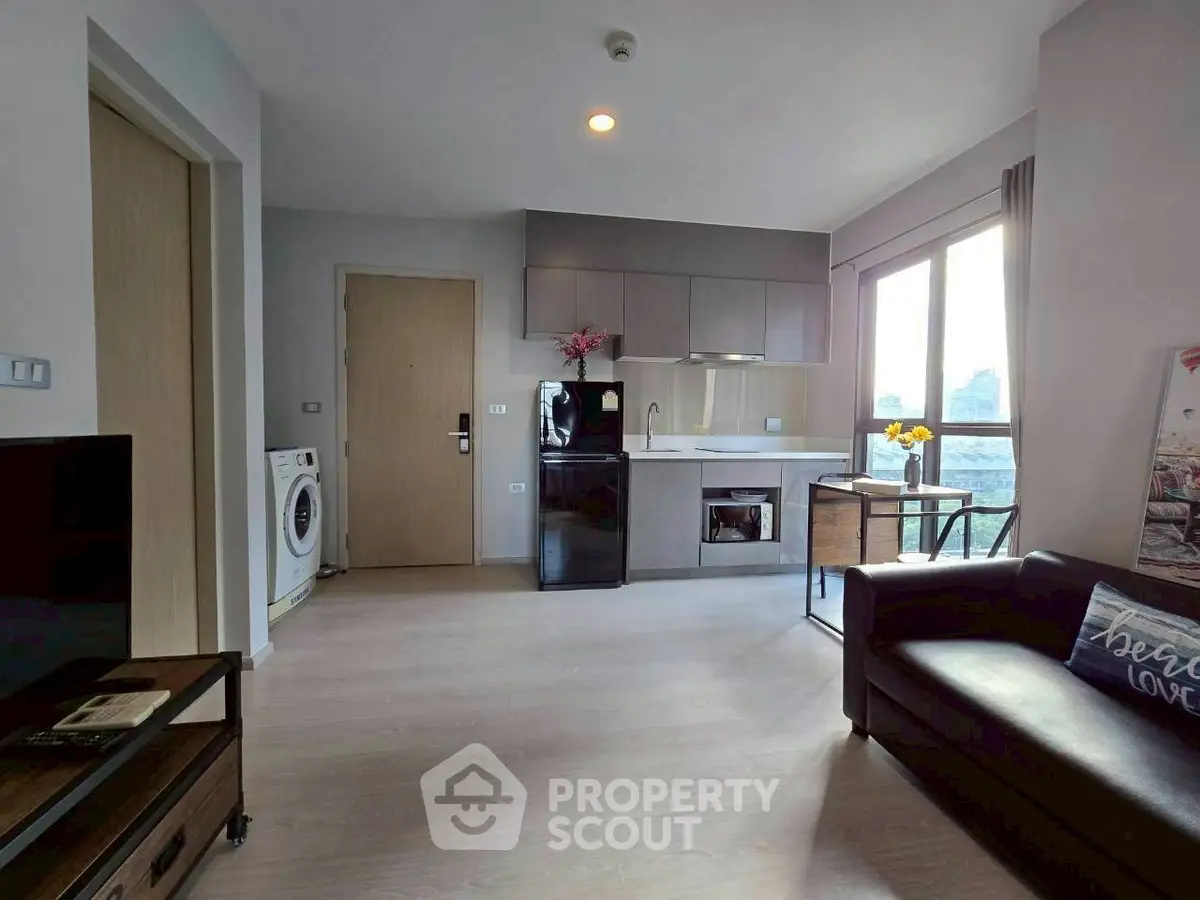 Modern living room with open kitchen and city view, featuring sleek appliances and cozy seating area.