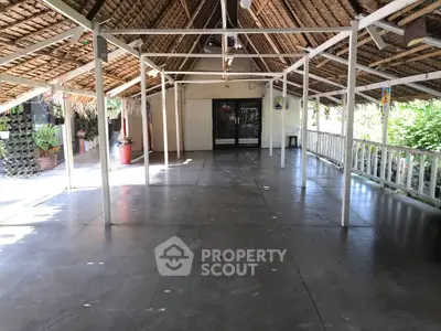 Spacious open-air terrace with rustic thatched roof and garden view, perfect for events or relaxation.