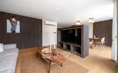 Spacious modern living room with wooden accents and open dining area, featuring a large TV and stylish furniture.