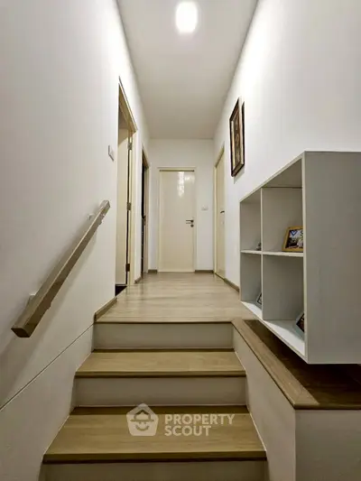 Modern hallway with wooden steps and built-in shelving, leading to multiple rooms.