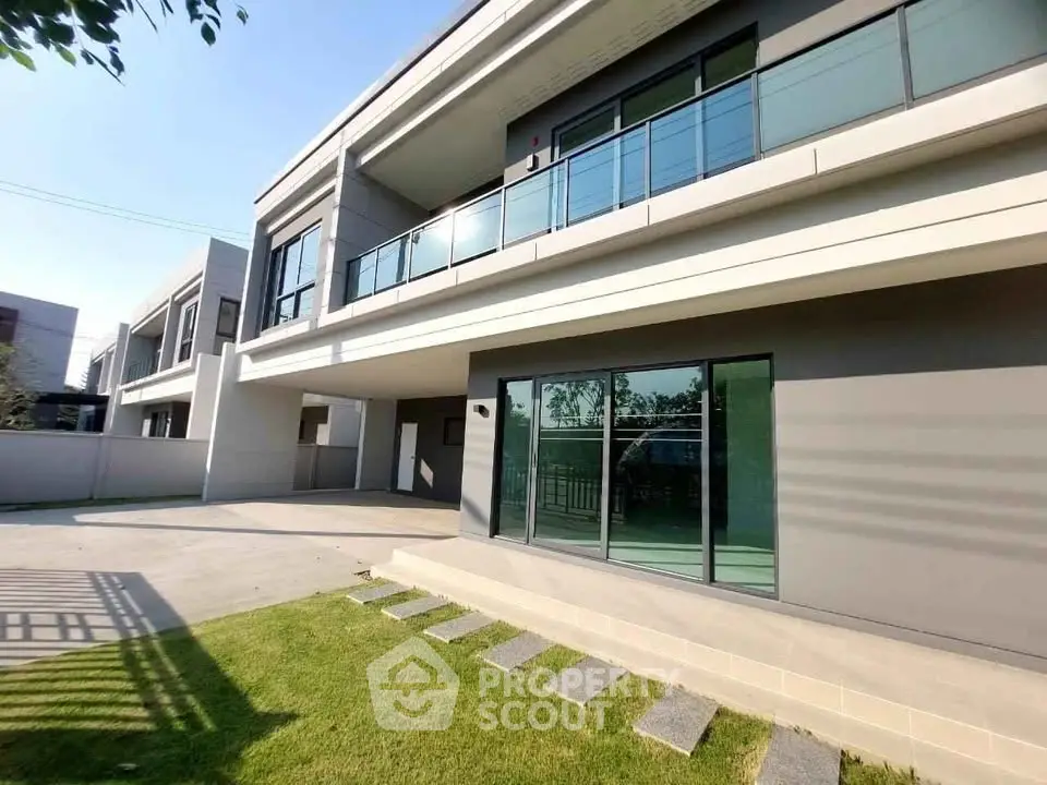 Modern two-story building with spacious balcony and large glass windows, surrounded by a lush green lawn.