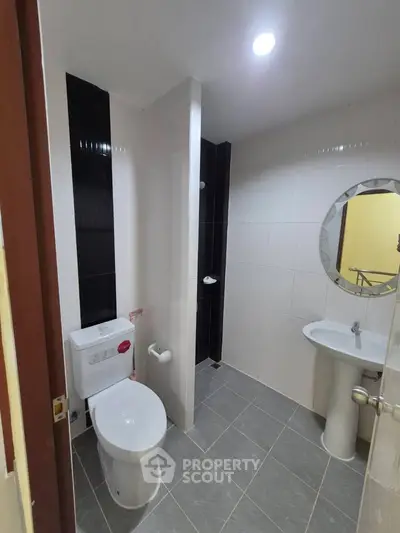 Modern bathroom with sleek design, featuring a round mirror and contemporary fixtures.