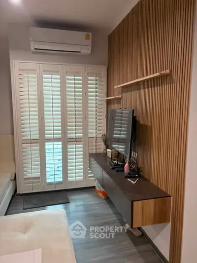 Modern living room with sleek wooden paneling and wall-mounted TV, featuring stylish shutters and air conditioning.