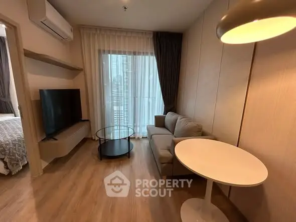 Modern living room with cozy sofa, round table, and large TV, featuring elegant wood flooring.