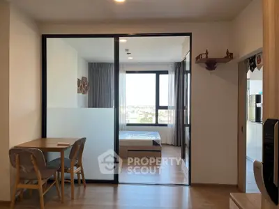 Modern apartment interior with glass partition, dining area, and bedroom view.