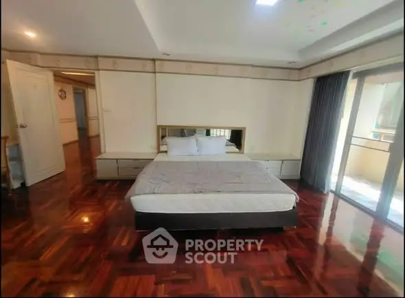 Spacious bedroom with hardwood floors and balcony access in modern apartment.