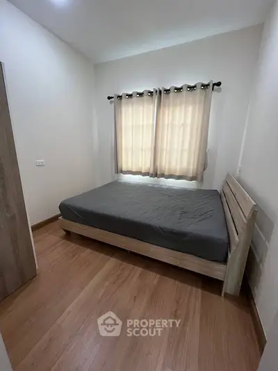 Cozy bedroom with wooden flooring and natural light through curtains.