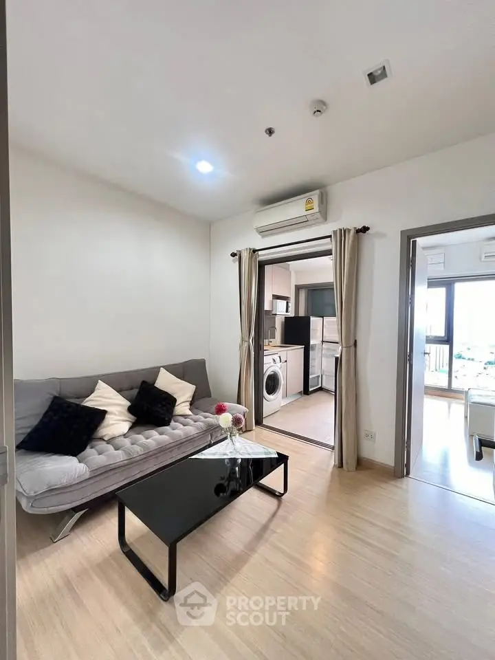 Modern living room with sleek sofa, open kitchen, and washing machine in a stylish apartment.